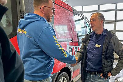 Zwei Männer begrüßen sich per Handschlag vor einem Fahrzeug in einer Werkstatt.Zwei Männer begrüßen sich per Handschlag vor einem Fahrzeug in einer Werkstatt.Zwei Männer begrüßen sich per Handschlag vor einem Fahrzeug in einer Werkstatt.Zwei Männer begrüßen sich per Handschlag vor einem Fahrzeug in einer Werkstatt.