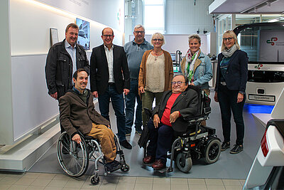 Viele Personen, zwei davon in einem Rollstuhl in Anzügen