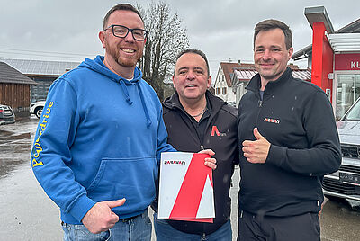 Drei Männer stehen im Freien und halten eine PARAVAN-Mappe; einer trägt einen blauen Hoodie mit „Powerdrive“-Schriftzug.