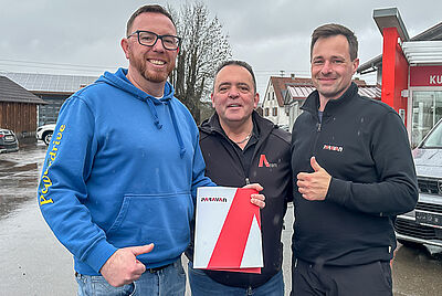 Drei Männer stehen im Freien und halten eine PARAVAN-Mappe; einer trägt einen blauen Hoodie mit „Powerdrive“-Schriftzug.