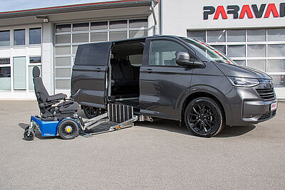 Ein grauer VW New Caravelle mit offener Hintertüre, einem herausgefahrenen Kassettenlift auf dem halb ein Rollstuhl drauf steht.