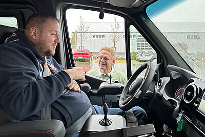 Roland Arnold im Gespräch mit einem Kunden, der in einem behindertengerecht umgebauten Fahrzeug mit Space Drive Steuerung sitzt.