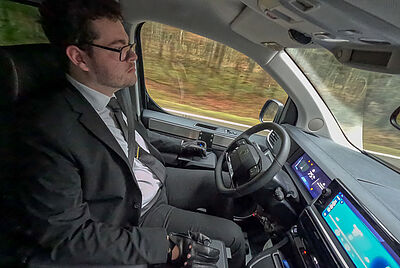 Fahrer mit Behinderung steuert ein umgebautes Fahrzeug mit Joystick-Fahrhilfe während der Fahrt.