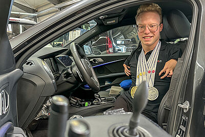 Josia Topf sitzt auf dem Fahrersitz seines angepassten Fahrzeugs und grinst in die Kamera. Um den Hals seine Medaillen der Paralympics.