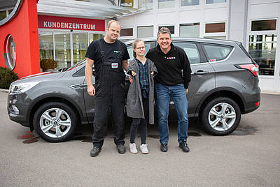 Zufriedene Paravan Kundin Marina steht stolz zusammen mit zwei tollen Mitarbeitern von Paravan vor Ihrem fertigen Auto