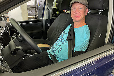 Mann ohne Arme sitzt am Steuer eines umgebauten Autos – PARAVAN Fusslenkung ermöglicht selbstständiges Autofahren.