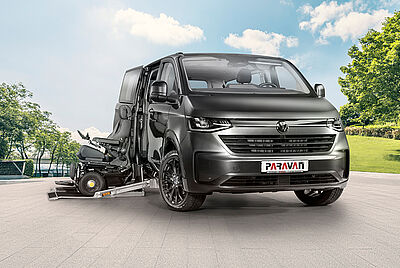 Eine VW New Caravelle in dunklem grau, steht mit geöffneter Seitentür, einem Herausgefahrenen Kassettenlift und einem davorstehenden PARAVAN Rollstuhl mit dunkelblauem Chassie, auf dem Hof der PARAVAN GmbH.