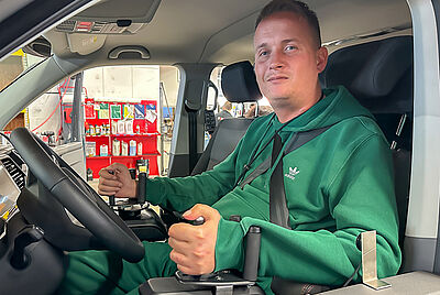Philip sitz mit seinem Rollstuhl auf der Fahrerseite seines neuen Fahrzeugs und blickt zum Seitenfenster hinaus, seine Hände liegen in den Space Drive Eingabegeräten.