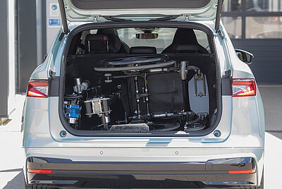 Ein Rollstuhl der in einem offenen Kofferraum seitlich drin liegt und mit dem Robot 3000 von Kofferraum zur Fahrertür befördert wird.