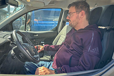 Ein Mann sitzt bei Sonnenschein, trotz Muskeldystropie, in seinem von PARAVAN umgebauten PKW mit dem Space Drive System. Er fährt über zwei Joysticks und ist somit wieder mobil.