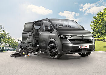 Der PARAVAN VW Caravelle Umbau steht an der Promenade eines Sees, davor ein blauer Elektrorollstuhl