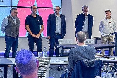 Eröffnung des Paravan Handicap-Seminars: Vier Personen stehen im Vordergrund vor dem Publikum und begrüßen die Teilnehmenden.