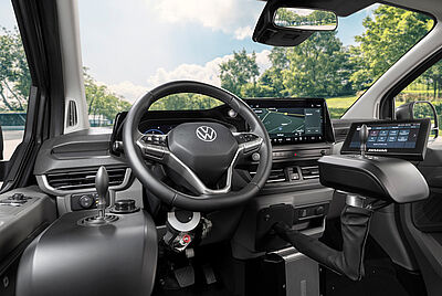 Ein Detailbild des Innenraus des neuen VW New Caravelle, bei dem man klare Sicht auf das Lenkrad hat, von der Fahrerseite aus. Etwas unscharf im Hintergrund sieht man ein eingebauter Paravan Joystick mit PARAVAN Touch Display.