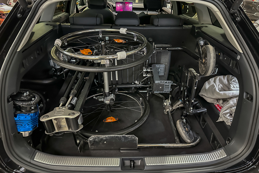Der Kofferraum eines schwarzen Fahrzeugs, indem links ein Robot 3000 verbaut worden ist. Ebenfalls befindet sich ein Aktivrollstuhl im Kofferraum, welcher der Robot 3000 hereingefahren hat. 