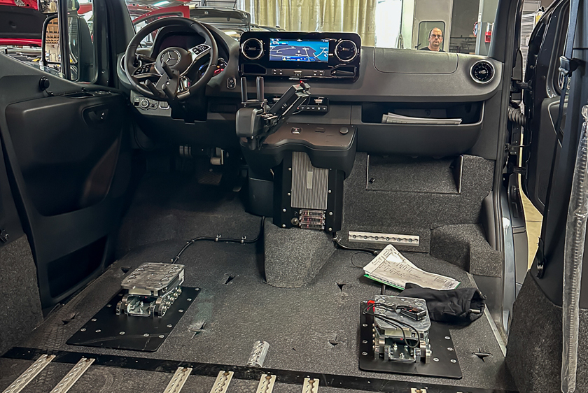 Der Fahrzeuginnenraum eines Autos bei dem sehr viel umgebaut wurde. Neben den Veränderungen am Lenkrad zur Steuerung des Fahrzeugs wurden sowohl der Fahrersitz sowie der Beifahrersitz entfernt und durch Dockingstation ersetzt. 