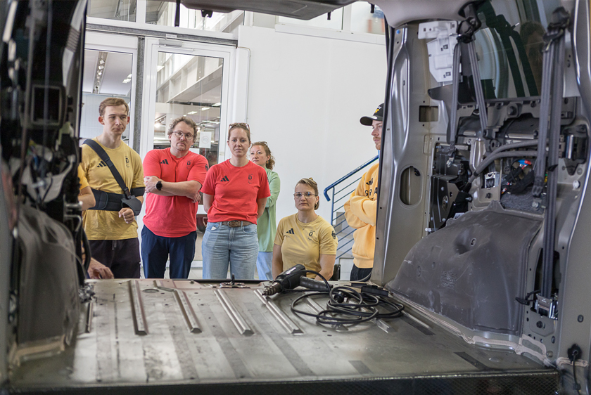 Durch ein leeres Auto, welches komplett ausgehöhlt worden ist schauen ein Paar Leute mit Team Deutschland Klamotten zum Heck hinein.