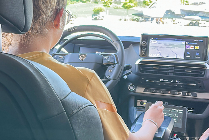 Eine Frau der man über die rechte Schulter schaut, fährt mit Joysticks ein Auto.