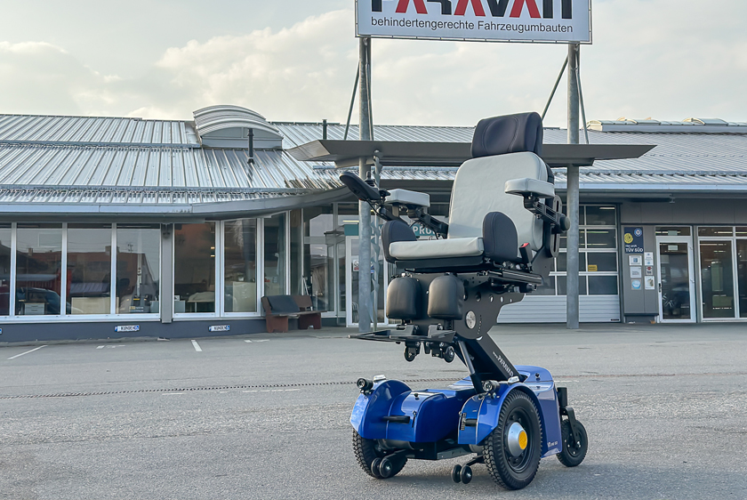Ein blauer Elektrorollstuhl, der PR50 steht auf dem Hof der Paravan GmbH und ist leicht nach oben gefahren worden.
