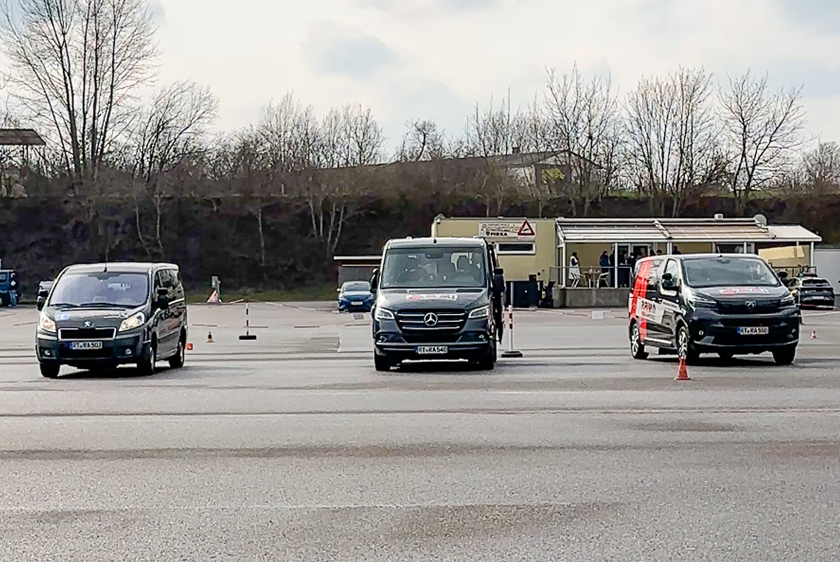 Drei Fahrzeuge stehen mit etwas viel Abstand nebeneinander, mit der Motorhaube frontal zur Kamera gerichtet. Das ganze auf einem großen Platz bei dem sich im Hintergrund ein kleines Haus sowie Bäume befinden.
