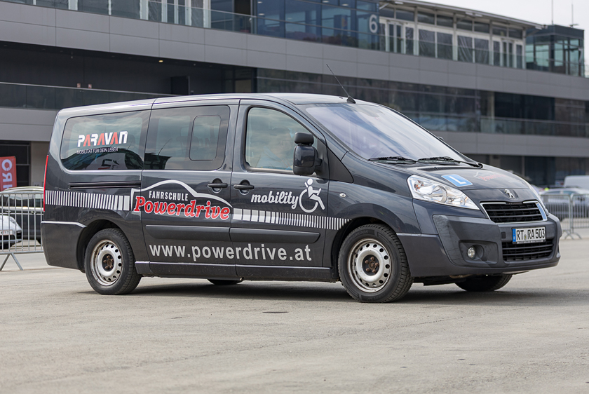 Ein graues Auto mit einer Beklebung der Powerdrive Fahrschule, sowie auf dem hintersten Seitenfenster einem Paravan Logo.