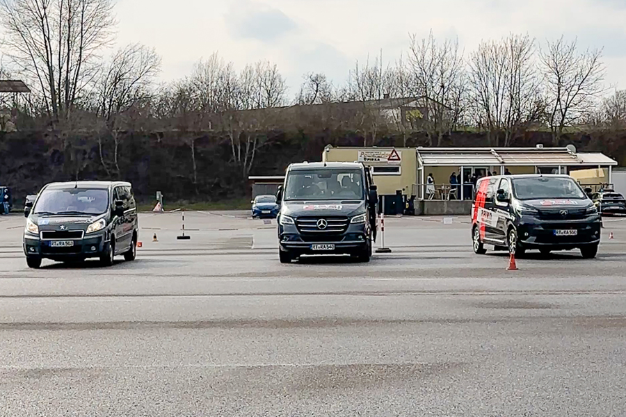 Drei Fahrzeuge stehen mit etwas viel Abstand nebeneinander, mit der Motorhaube frontal zur Kamera gerichtet. Das ganze auf einem großen Platz bei dem sich im Hintergrund ein kleines Haus sowie Bäume befinden.
