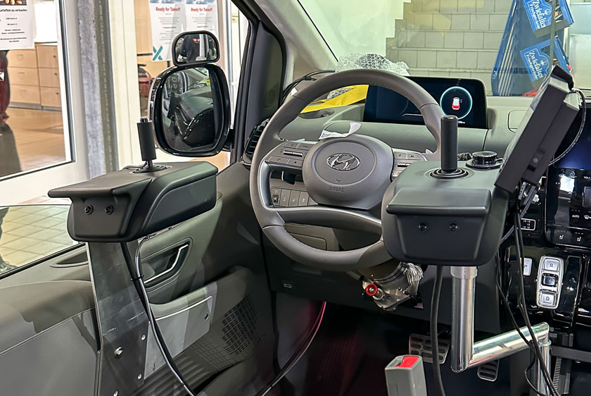 Rechts und Links neben einem Lenkrad in einem Fahrzeug befinden sich zwei Joysticks verbaut. Am rechten Joystick befindet sich ebenfalls ein Paravan Touch Diplay.