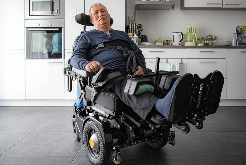 Ein älterer Mann sitzt in seinem PR40 Elektrorollstuhl mit ausgestreckten Füßen, also einem hochgefahrenen Fußbrett, entspannt in seiner Küche.