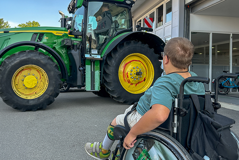 Rollstuhlfahrer betrachtet einen von PARAVAN umgebauten John Deere Traktor vor der Werkstatt.