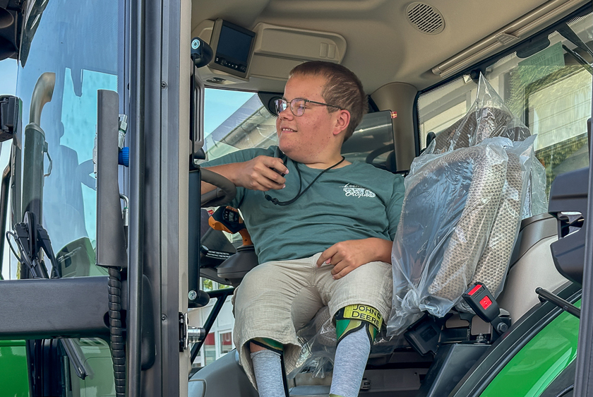 Junger Mann sitzt bei geöffneter Kabinentür auf dem Fahrersitz des individuell umgebauten John Deere Traktors.