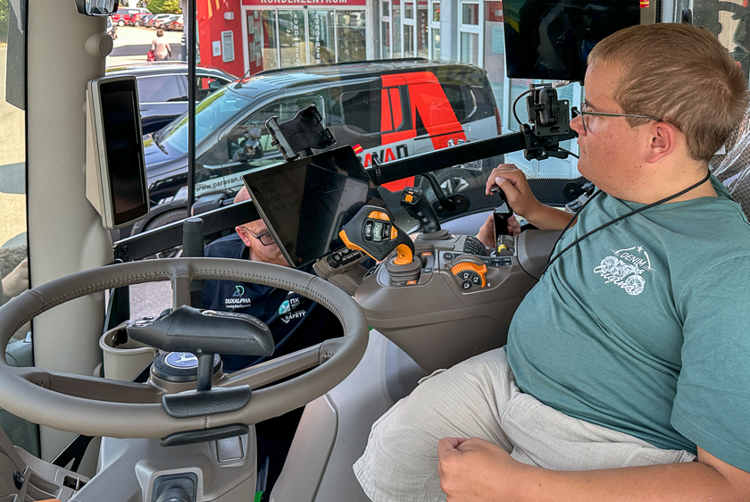 Junger Mann bedient den umgerüsteten John Deere Traktor über eine individuell angepasste Steuerung.
