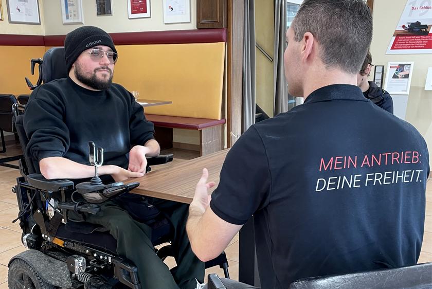 Links ein Kunde im Rollstuhl, der sich von einem Paravan Mitarbeiter rechts Beraten lässt, im Paravan Kundenzentrum. 